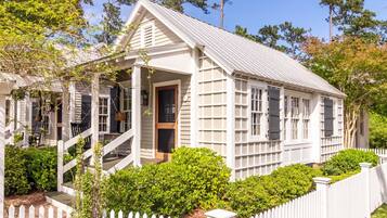 A white colonial-style house with a porch, a picket fence, and a well-maintained garden.