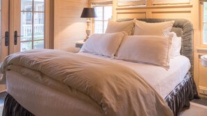 A bedroom with a large bed, wooden walls, and a window with blinds.