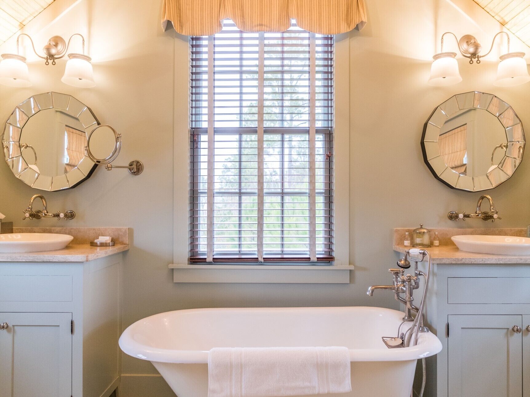 A bathroom with two sinks, a large bathtub, and a window with blinds.