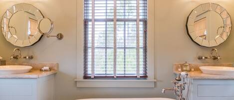 A bathroom with two sinks, a large bathtub, and a window with blinds.