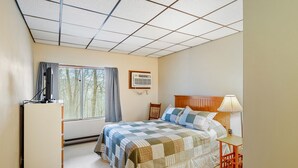 Un dormitorio con cama, escritorio, silla, televisor y ventana con cortinas.