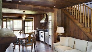 A rustic kitchen with wooden walls, a dining area with a table and chairs, and a staircase. - Grand Banks Cottage w/Full Kitchen - River Dunes (Oriental)