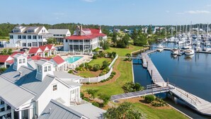 A marina with multiple boats docked, a large house with a red roof, and a swimming pool. - Grand Banks Cottage w/Full Kitchen - River Dunes (Oriental)