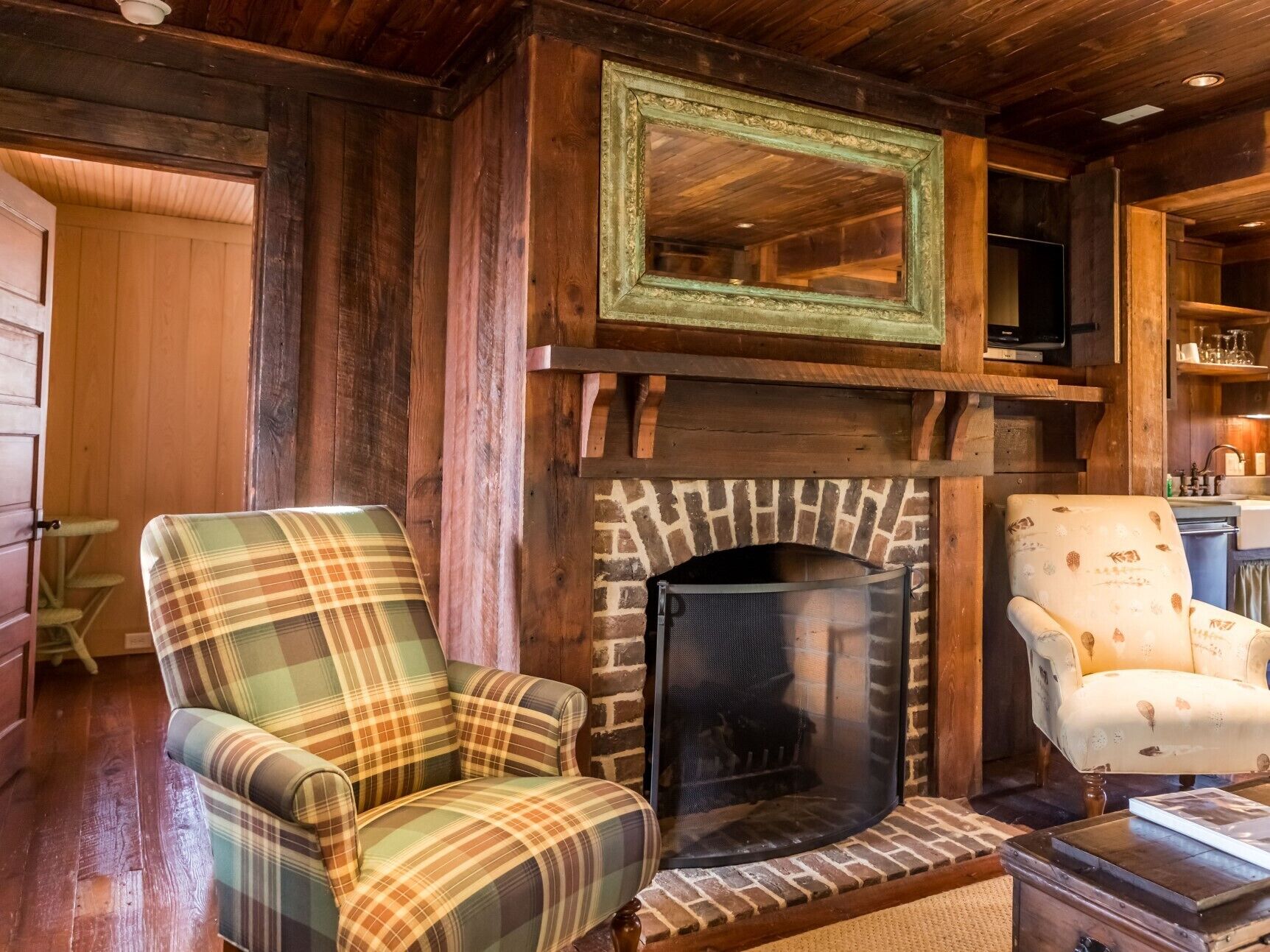 A cozy living room with a fireplace, plaid armchairs, and wooden walls.
