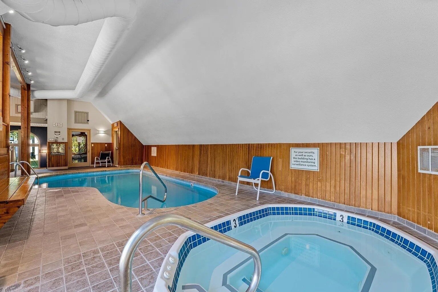 Une piscine intérieure divisée en deux zones distinctes, avec des murs en bois et une chaise bleue.