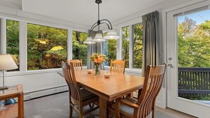 A dining area with a wooden table and chairs, a chandelier, and large windows with a view of trees. - Fall Line Condo D6 3 Bedroom Condo (Killington)