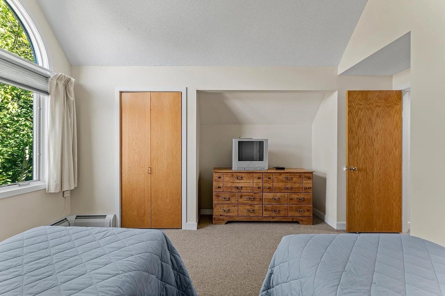 A bedroom with two beds, a wooden dresser, a television, and a window with curtains.