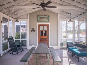 A covered porch with a wooden table and benches, a ceiling fan, and a view of the outside.