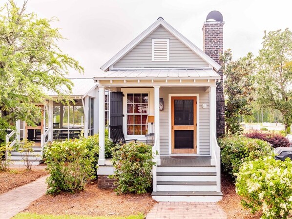 A small, single-story house with a porch, a chimney, and a garden.