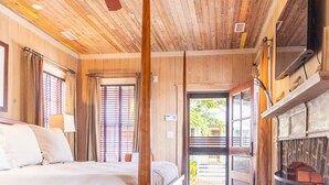 A wooden-paneled bedroom with a bed, a fireplace, and a view through a door.