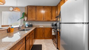 A kitchen with wooden cabinets, a stainless steel refrigerator, a microwave, and a sink. - Maui Kamaole, #a-106 1 Bedroom Condo (Kihei)