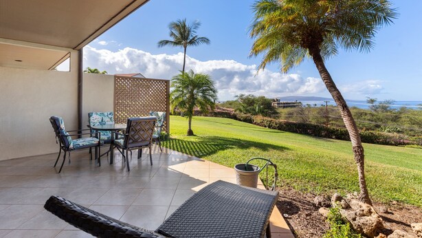 An outdoor patio with a table and chairs, a palm tree, and a view of the ocean. - Maui Kamaole, #a-106 1 Bedroom Condo (Kihei)