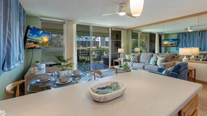 Una sala de estar moderna con un televisor grande, un comedor con mesa y sillas, y una zona de estar acogedora con un sofá y cojines.