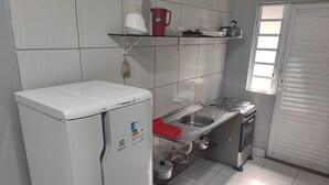 Eine kompakte Küche mit einem weißen Kühlschrank, einer Edelstahl-Spüle und einem Fenster mit Jalousien.