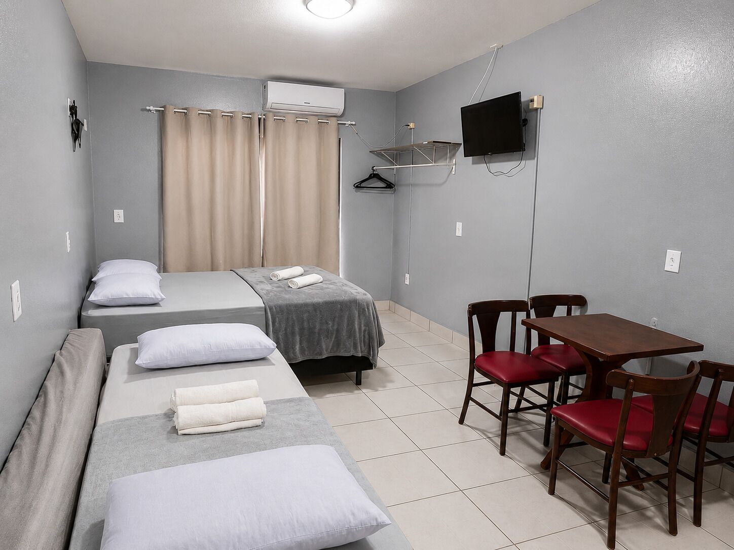 Una habitación con cama, una mesa con sillas, televisor y aire acondicionado.