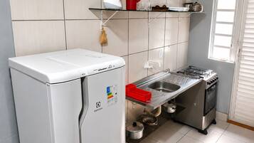 A compact kitchen with a refrigerator, stove, sink, and a window with blinds.