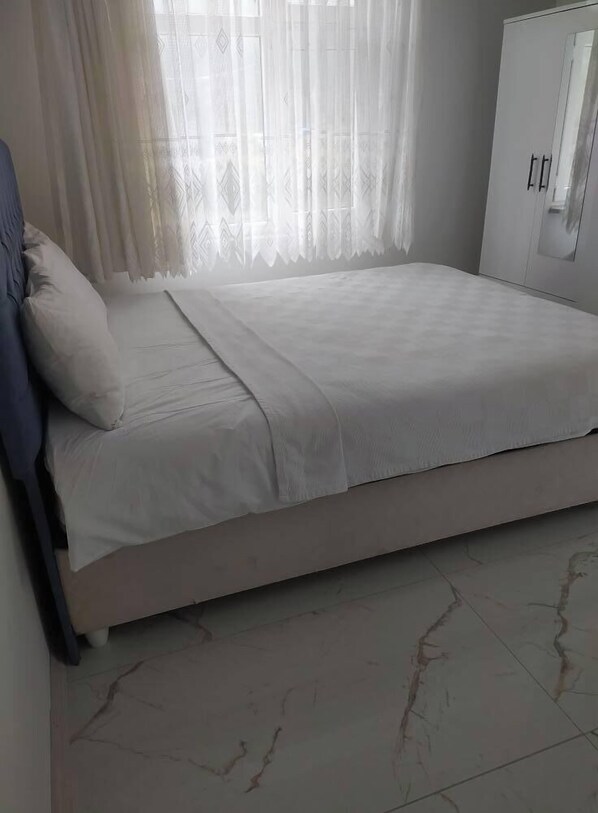 Un dormitorio con cama, armario y ventana con cortinas.