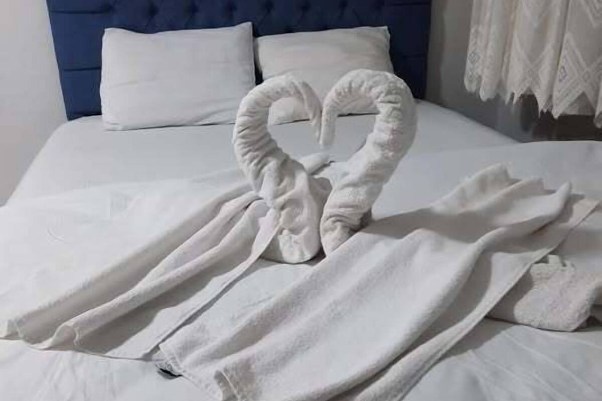 A bed with a blue headboard, white pillows, and a towel arranged in a heart shape on the bed.