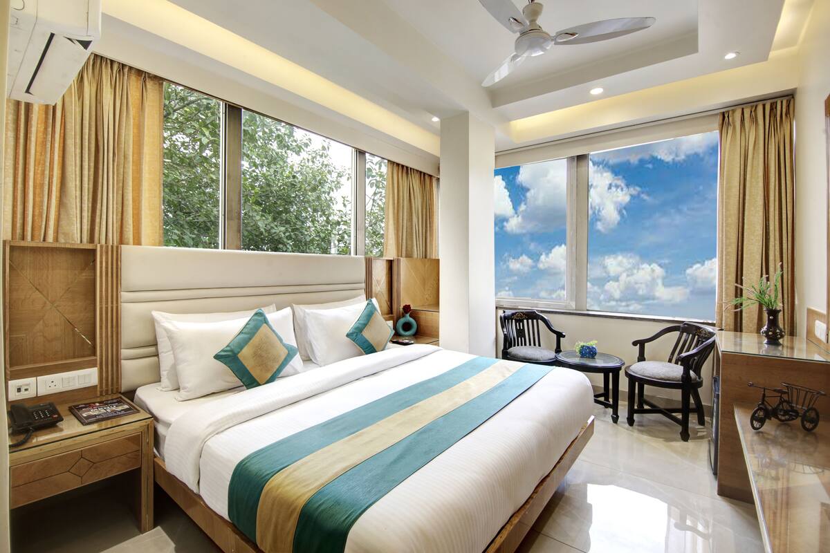 Une chambre d’hôtel avec un grand lit, un bureau avec une chaise, une petite table et une fenêtre donnant sur le ciel.