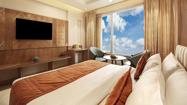 Een hotelkamer met een groot bed, een tv aan de muur, een bureau met een stoel, en een raam met uitzicht op de lucht.