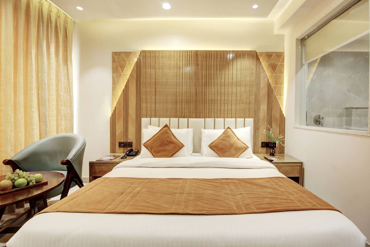 Une chambre d’hôtel avec un grand lit, une tête de lit en bois, une table de chevet avec une lampe et une fenêtre donnant sur un beau paysage.