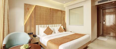 Habitación de hotel con una cama grande, un cabecero de madera, un escritorio con una silla y una mesa de comedor con fruta.