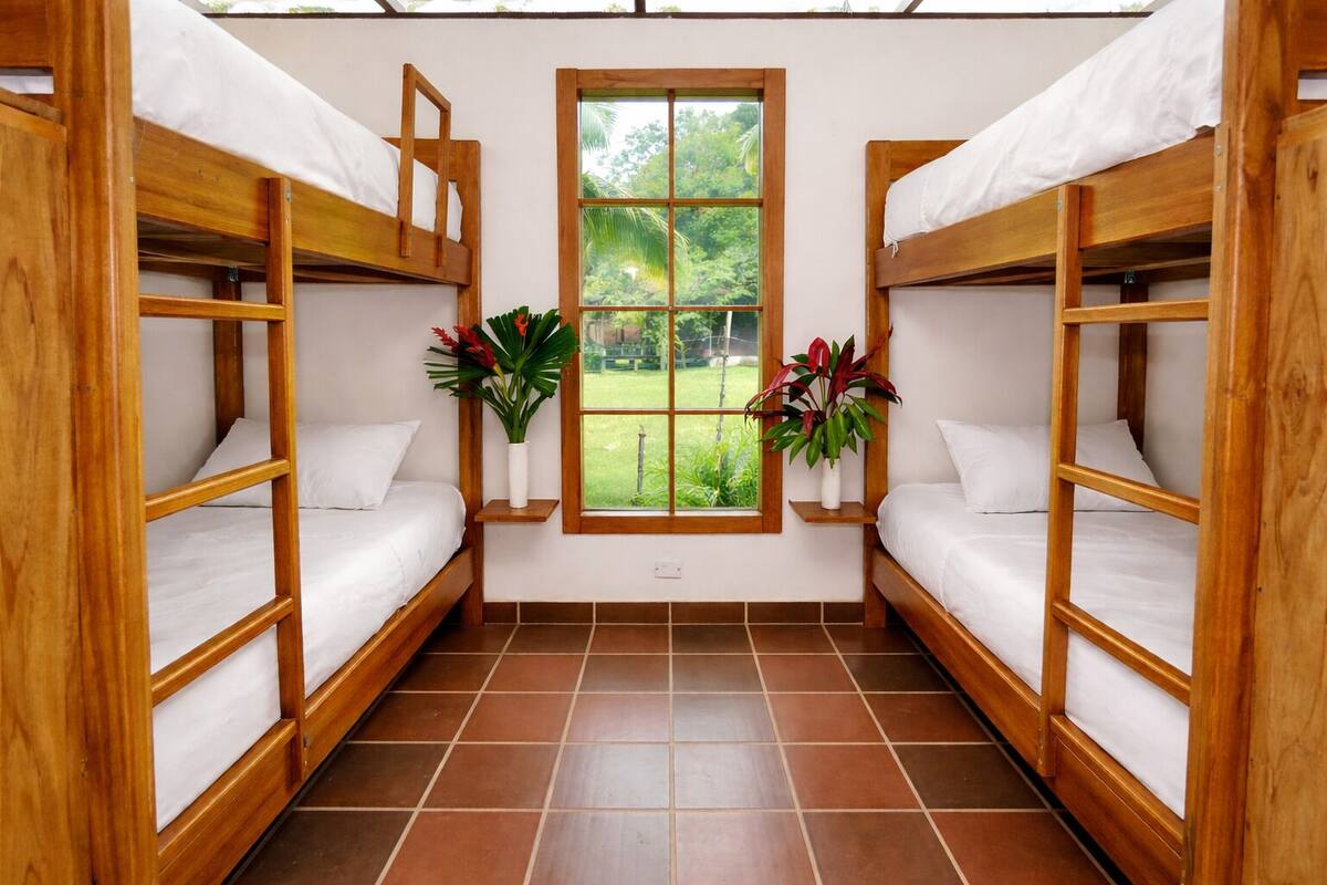 Ein Zimmer mit zwei Holzbettklappen, einem Fenster mit Blick auf Grünflächen und zwei Blumentöpfen.