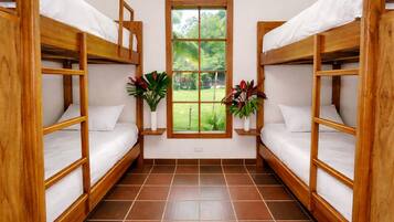 Una habitación con dos camas litera de madera, una ventana que da a zonas verdes y dos plantas en macetas.