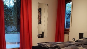 Een slaapkamer met een bed, een grote spiegel en uitzicht op een tuin door een raam.
