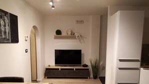 Een moderne woonkamer met een flatscreen televisie, een eettafel en een keuken met een koelkast.
