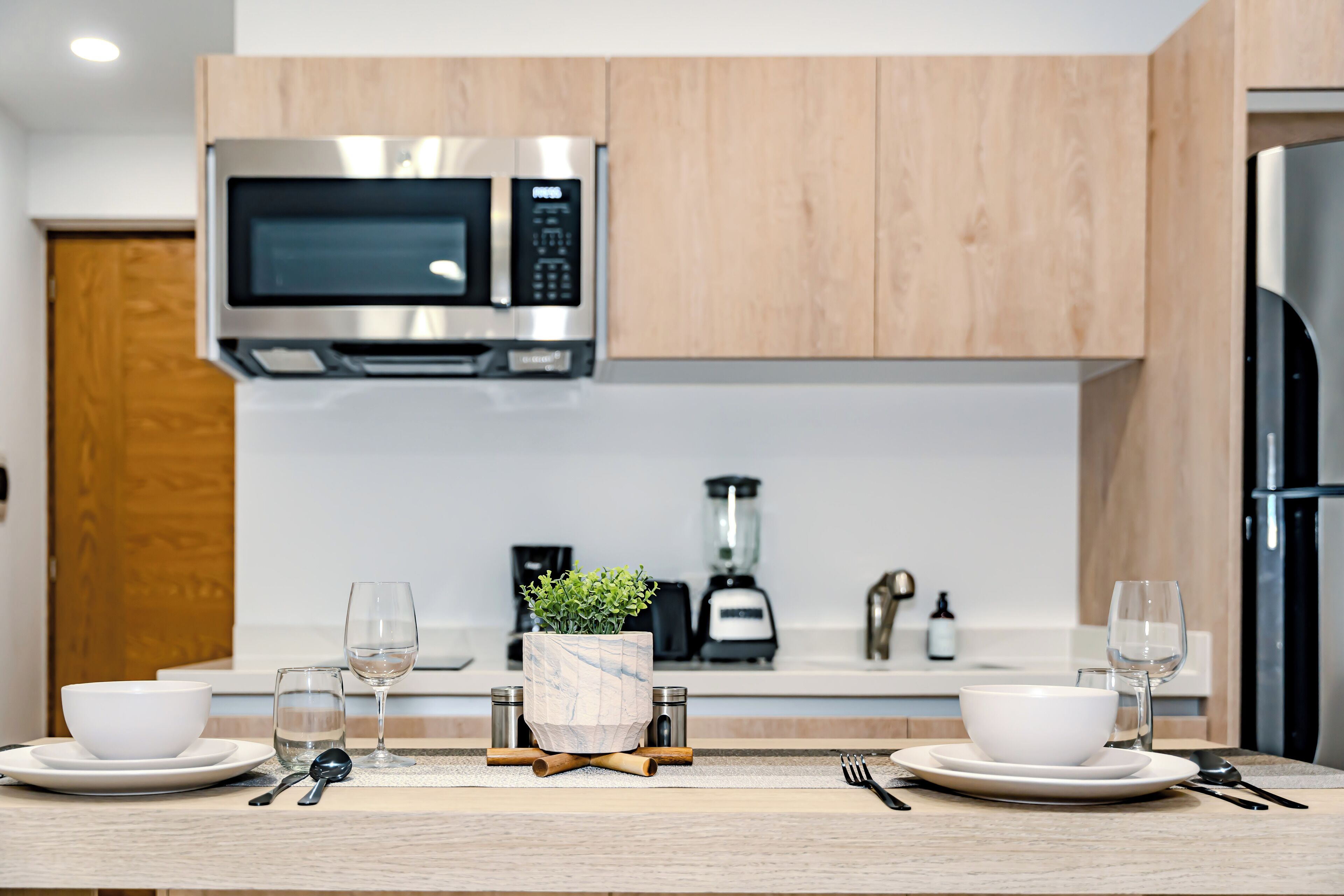 Une cuisine moderne avec des meubles en bois, un four à micro-ondes en acier inoxydable, un mixeur et un réfrigérateur.