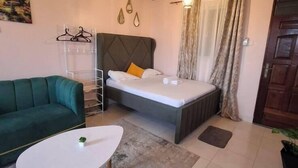 Een slaapkamer met een bed, een groene bank, een witte salontafel en een plafondventilator.