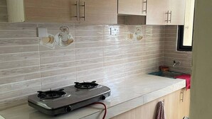 Een moderne keuken met lichte houten kastjes, een gasfornuis en een betegelde spatwand.