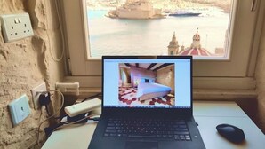 A laptop on a desk with a view of a coastal city through a window.