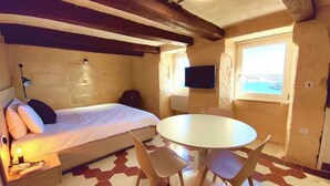 A compact bedroom with a bed, a round table, and chairs, a TV, and a window with a view.