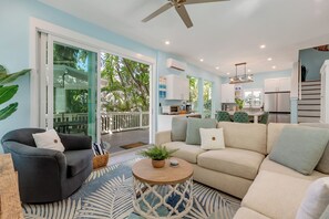 A spacious living area with a sofa, armchairs, and a coffee table. There is a sliding glass door leading to a balcony with a view of greenery. - INTO THE BLUE~GRAND OPENING RATES! Pristine 4 BR/3.5 BA Home w/Private Pool! (Key West)