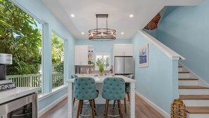 A modern kitchen with white cabinets, a stainless steel refrigerator, and a teal upholstered dining area.