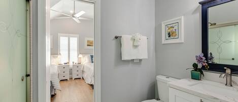 A bathroom with a toilet, sink, and mirror. There is a towel hanging on the wall and a ceiling fan above the toilet.