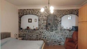 Un dormitorio con pared de piedra, una cama, una silla y una chimenea.