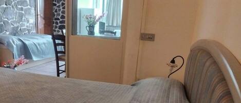A bedroom with a large bed, a stone wall, a television, and a view of a dining area.