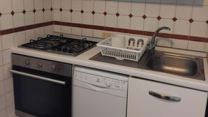 Una cocina compacta con armarios blancos, una estufa a gas, horno, lavavajillas y pileta.