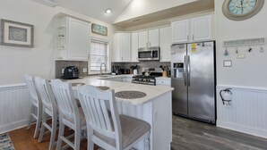 A kitchen with white cabinets, a stainless steel refrigerator, a microwave, and a coffee maker. There are four white chairs around a central island. - 3-bedroom condo in delightful Ocean City with WiFi, AC (Ocean City)