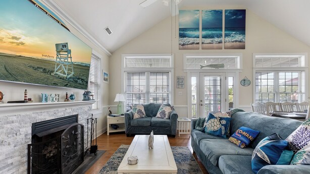 A spacious living room with a fireplace, a large TV displaying a beach scene, a grey sofa with colorful cushions, and a white coffee table. - 3-bedroom condo in delightful Ocean City with WiFi, AC (Ocean City)