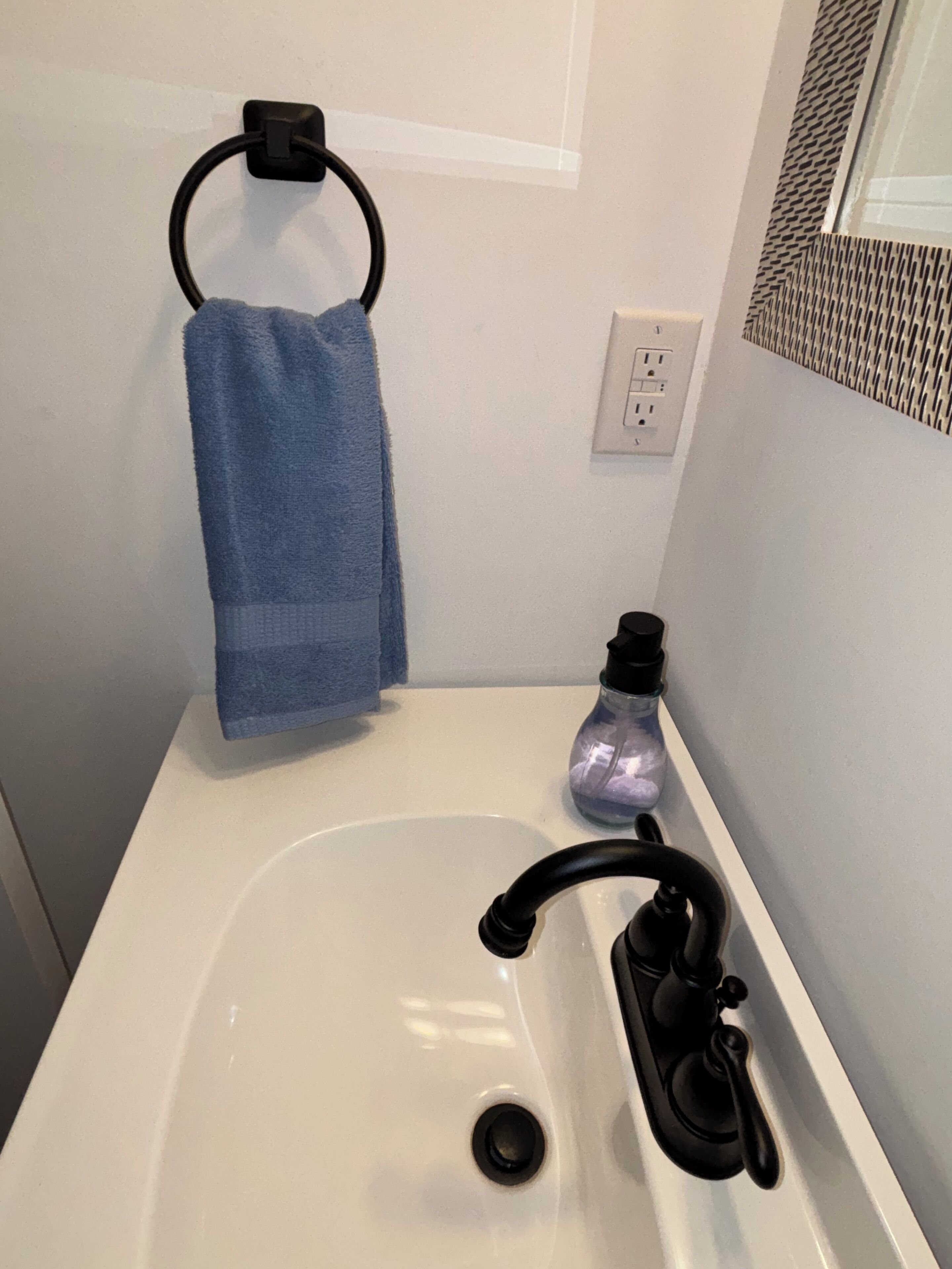 Un bagno con un lavandino bianco, un rubinetto nero e un asciugamano blu appeso a un porta-asciugamani nero, oltre a un dispenser per sapone.