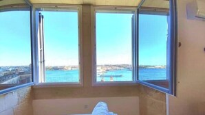 Ein Zimmer mit Bett und Blick auf das Meer sowie die Stadt durch große Fenster.