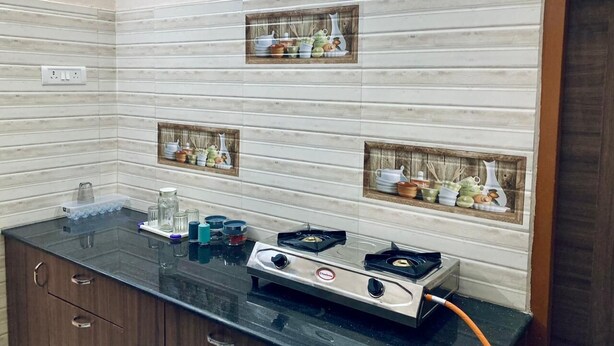 A kitchen with a black countertop, a gas stove, and three wooden-framed shelves with kitchenware. - GOOD STAY serviced apartments egmore   (Chennai)