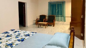 A bedroom with a bed, two chairs, a wooden door, and a ceiling fan. - GOOD STAY serviced apartments egmore   (Chennai)