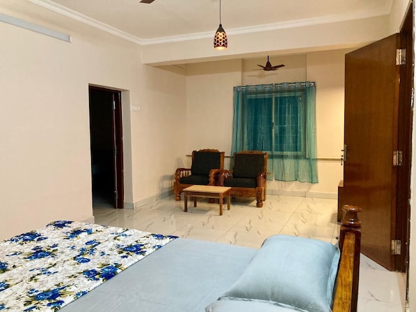 A bedroom with a bed, two chairs, a wooden door, and a ceiling fan.