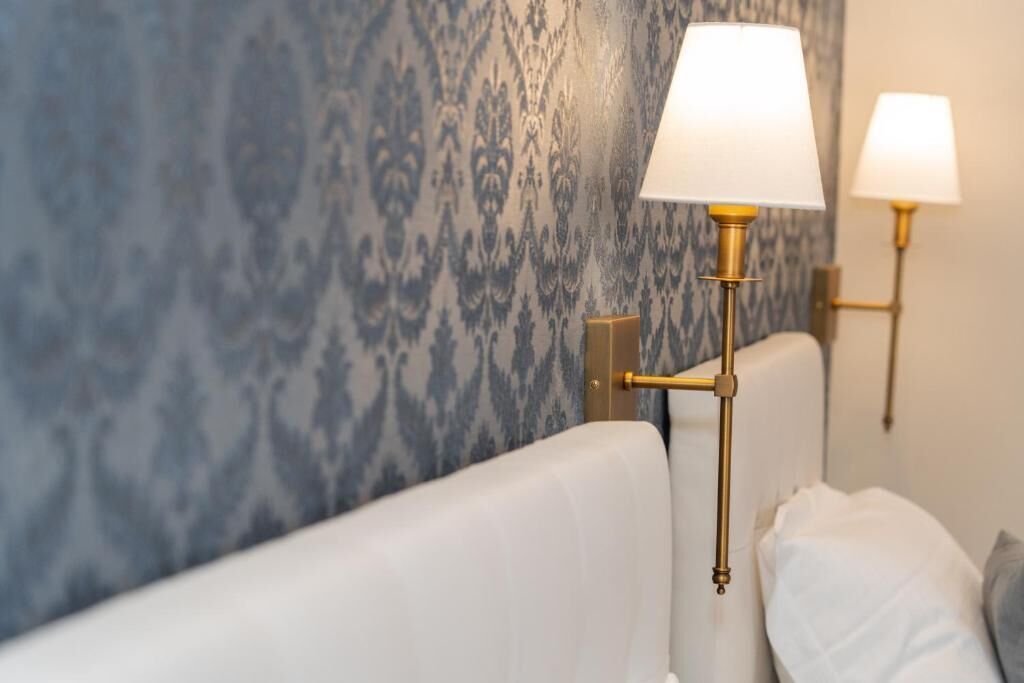 A room with a patterned wallpaper, a white sofa, and two wall-mounted lamps with white shades.