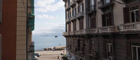 A street view with a building featuring multiple balconies and a clear view of the sea.